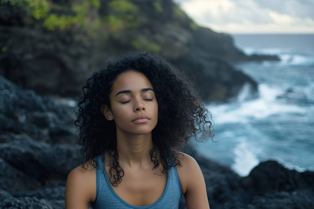 Serene Woman Meditating on Rocky Ocean Cliffside with Eyes Closed.